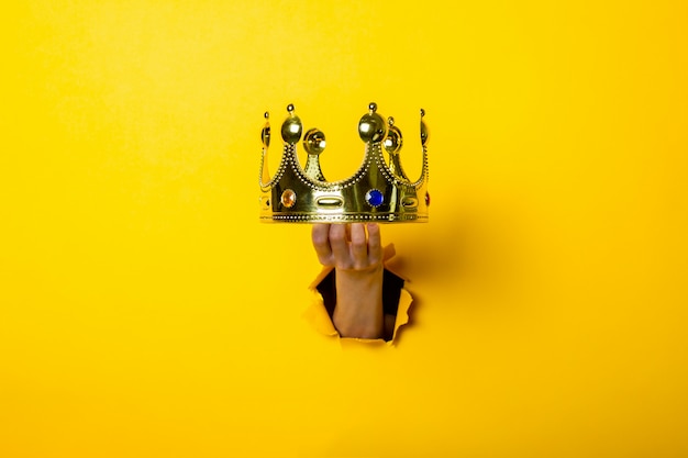 Female hand holds a gold crown on a bright yellow background