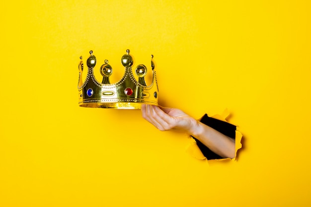 Female hand holds a gold crown on a bright yellow background