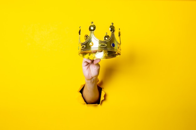 Female hand holds a gold crown on a bright yellow background