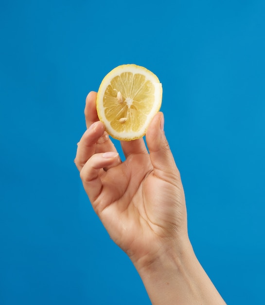 Female hand holds half a yellow lemon and squeezes it