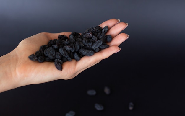 Female hand holds a handful of raisins on black