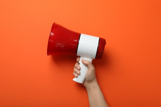 Female hand holds megaphone on orange background