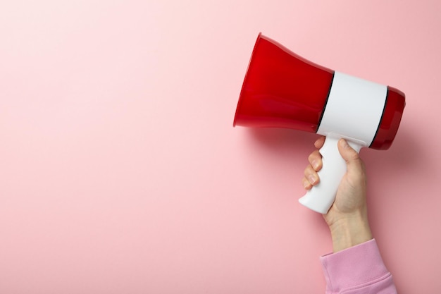 Female hand holds megaphone on pink background