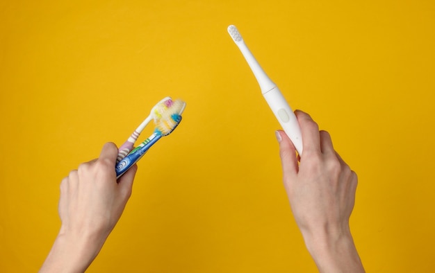 Female hand holds a modern electro-toothbrush with charger on  yellow.