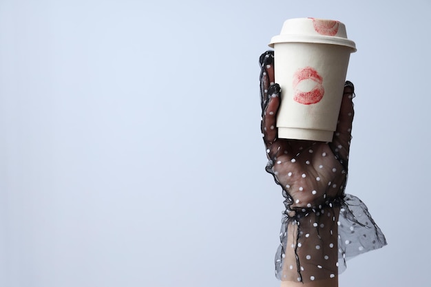 Female hand holds paper cup with kisses on white background