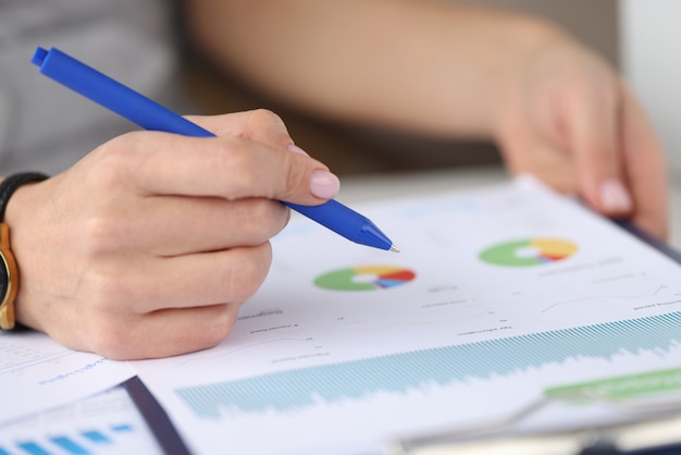 Female hand holds pen over graph with business records. Business reporting and development