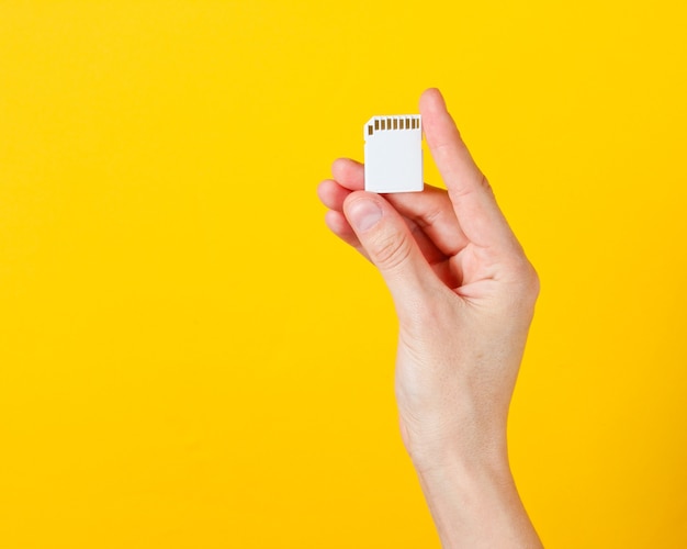 Female hand holds SD memory card on yellow. Minimalist Techno Concept.