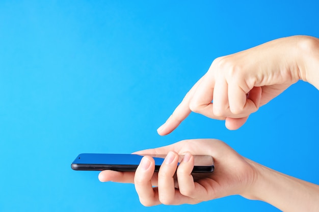 Female hand holds smartphone on blue background. Woman touch mobile display with finger