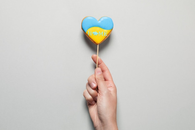 Female hand holds stick with cookie with Ukraine flag colors on gray background