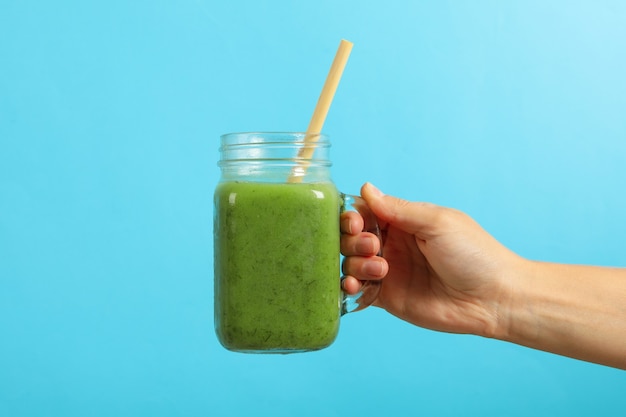 Female hand holds vegetable smoothie on blue background