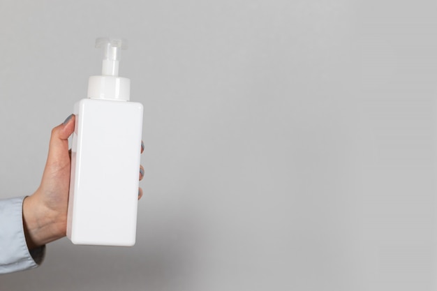 Female hand holds a white plastic bottle with antibacterial soap sanitizer on a gray background. Coronavirus and pandemic protection agent.