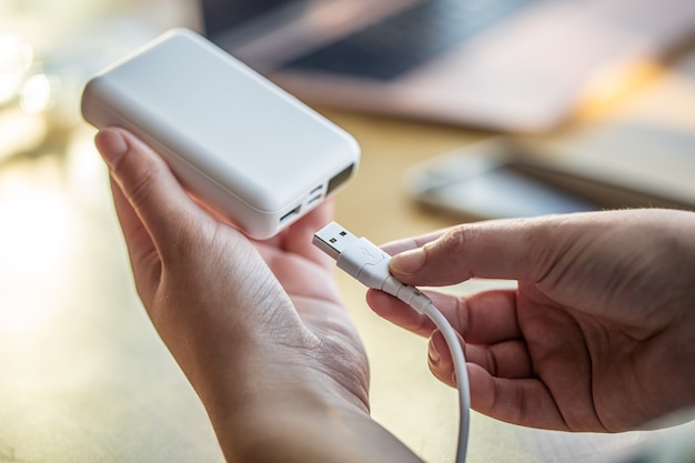 A female hand holds a white USB cable and a white power bank, charging the phone using a power bank.