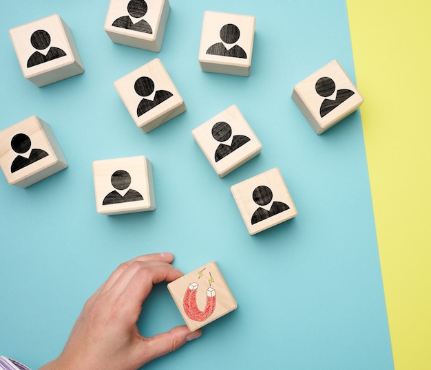 Female hand holds a wooden cube with a magnet and wooden cubes with little men, recruiting for a strong team. Open vacancies in the company, flat lay