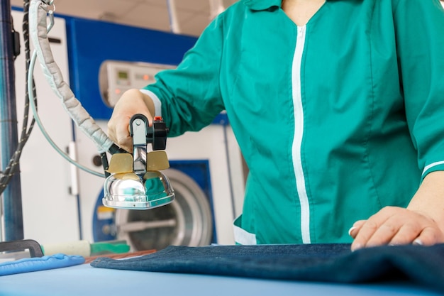 Female hand ironing blue jeans in a dry cleaning service