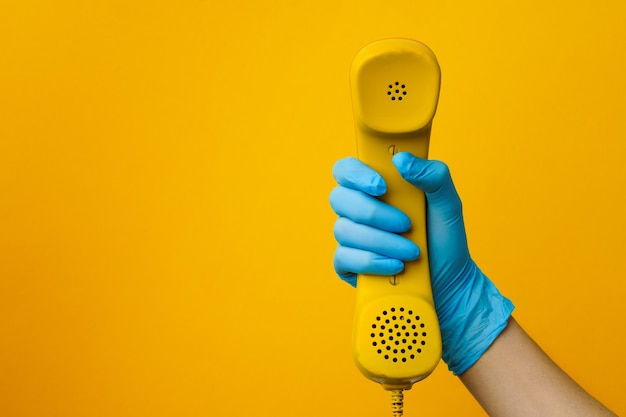 Female hand in medical glove holding yellow telephone speaker