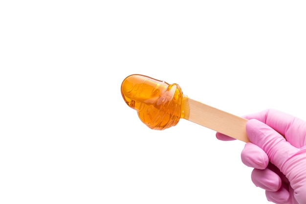 A female hand in a pink glove holds a wooden stick with sugar paste for depilation