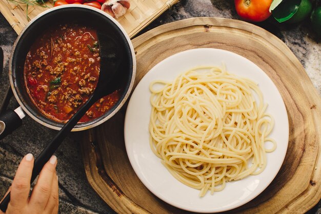 Female hand pouring tomato sauce into a plate of pasta top view