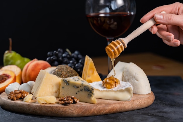 A female hand pours honey on camembert with walnuts using a special honey spoon. An exquisite combination of expensive delicacies.