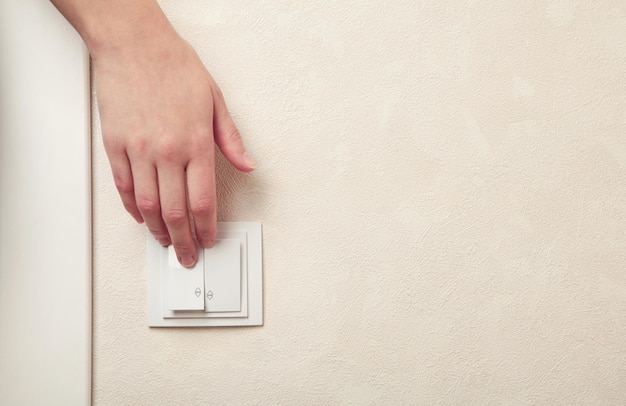 Female hand pressing light switch in apartment closeup