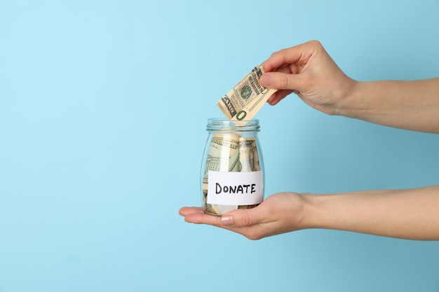 Female hand puts money in glass jar on blue  space