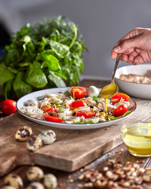 Female hand puts mustart sause to the plate of freshly cooked homemade salad from natural ingredients on a wooden table.