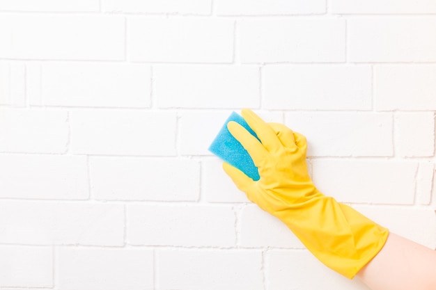 A female hand in a rubber glove holds a blue paralonne sponge for cleaning and washing dishes