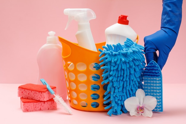 Female hand in a rubber glove with bottles of dishwashing liquid, glass and tile cleaner, detergent for microwave ovens and stoves, rag, brushes and sponges. Washing and cleaning set.