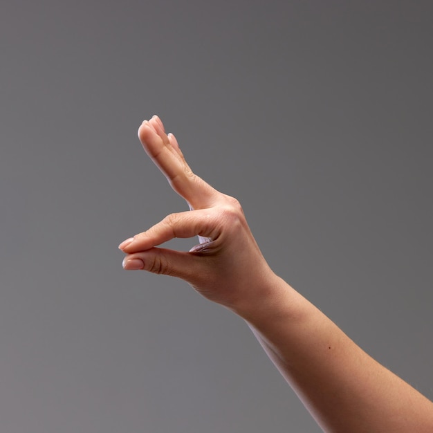 Female hand showing gesture against grey background playing with gestures making figures with