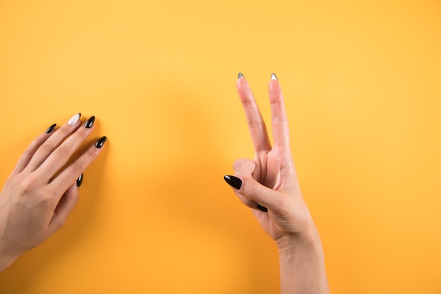 Female hand shows peace sign on orange background