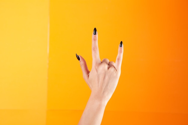 Female hand shows rock sign on orange background