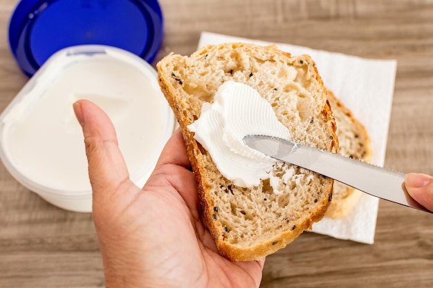 Female hand spreading white cheese on a slice of bread on a wooden table