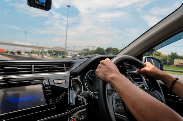 Female hand on the steering wheel driving a car on the road.