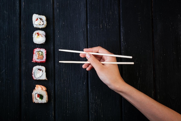 Female hand takes chopsticks sushi rolls with Chinese chopsticks Lying on a black wooden board View from above