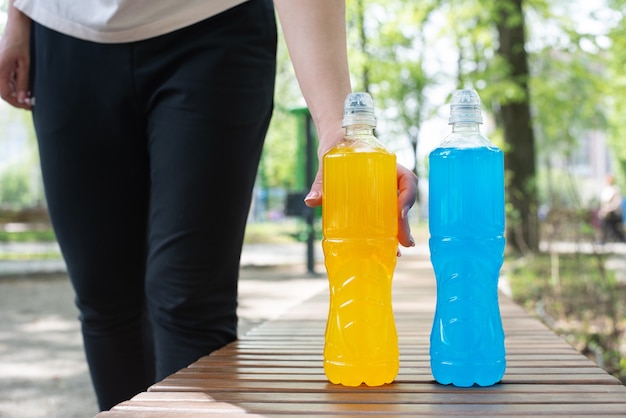 Female hand taking a bottle of isotonic drink during a break in training for the restoration of water-salt balance in the street, summer, close up.