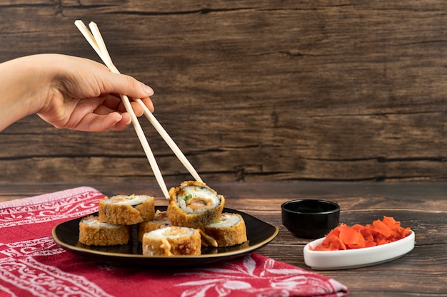 Female hand taking hot sushi roll with chopsticks on wooden surface. 