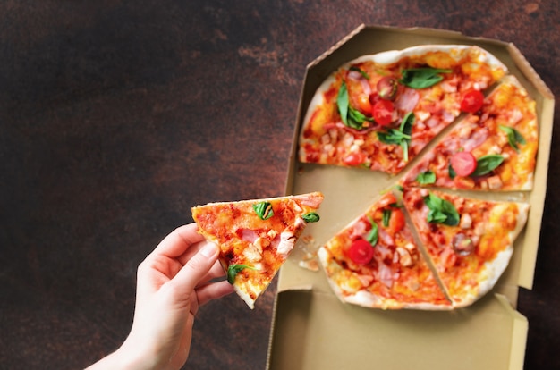 Female hand taking slice of fresh pizza from delivery box. 