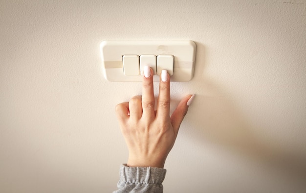 Female hand turning an electricity light switch on the wall.