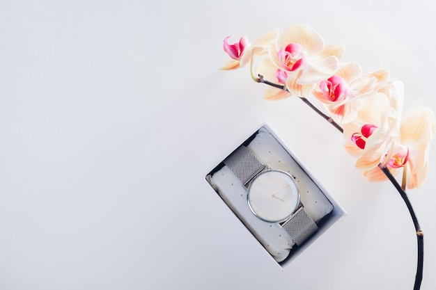 Female hand watch in gift box surrounded with orchid Present for Women's day