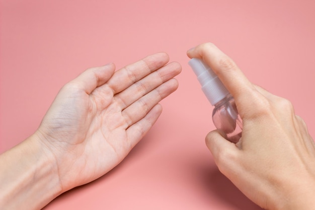 Female hand with an antiseptic applies liquid to the palm on a pink background close-up. The concept of hygiene and cleanliness. Disinfectant.