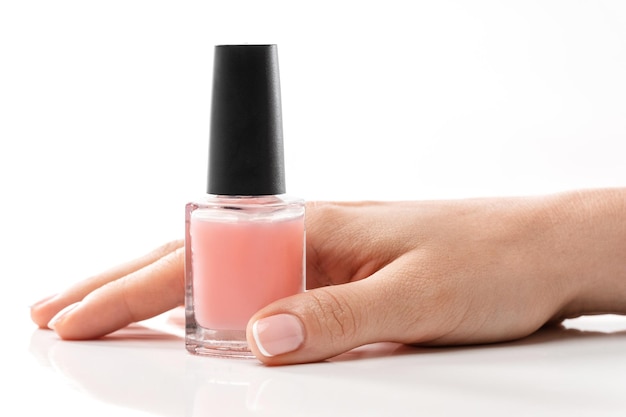 Female hand with beautiful french manicure holding bottle of pink nail polish against white background