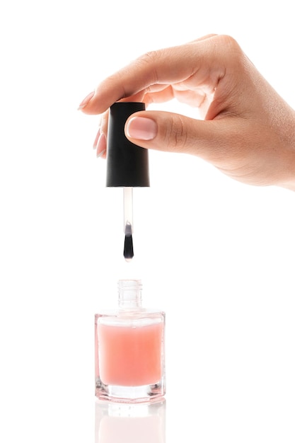 Female hand with beautiful french manicure holding bottle of pink nail polish against white background