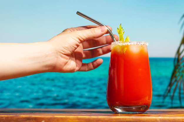 Female hand with bloody Mary cocktail on tropical beach