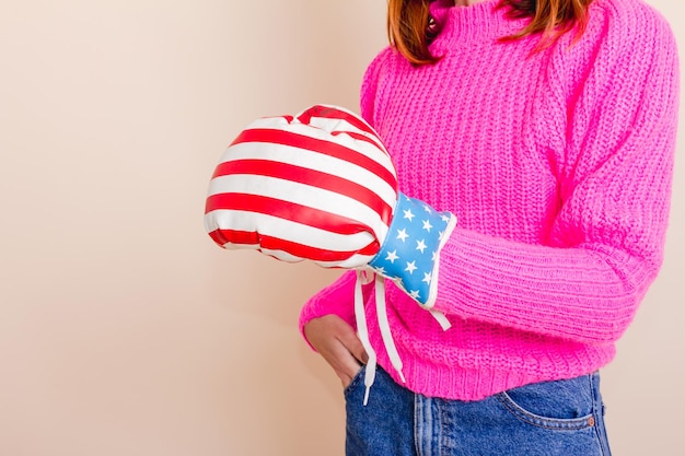 Female hand with boxing glove with US flag design. Studio shot with light yellow background.