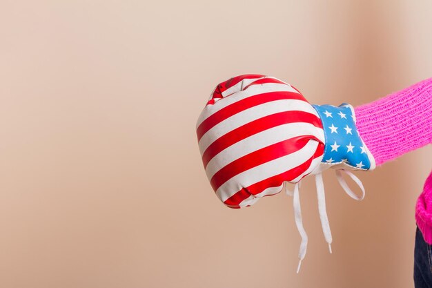 Female hand with boxing glove with US flag design. Studio shot with light yellow background.