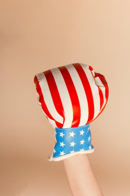 Female hand with boxing glove with US flag design. Studio shot with light yellow background.