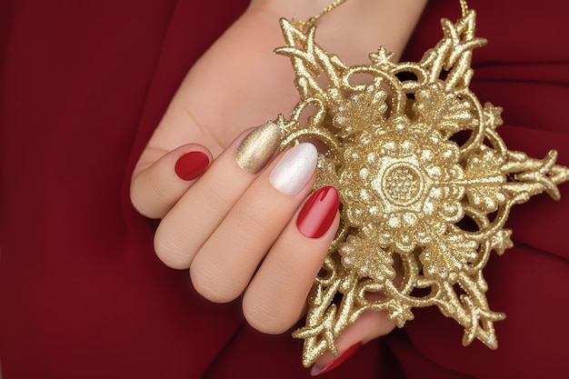 Female hand with Christmas nail design holding a golden New Year star.