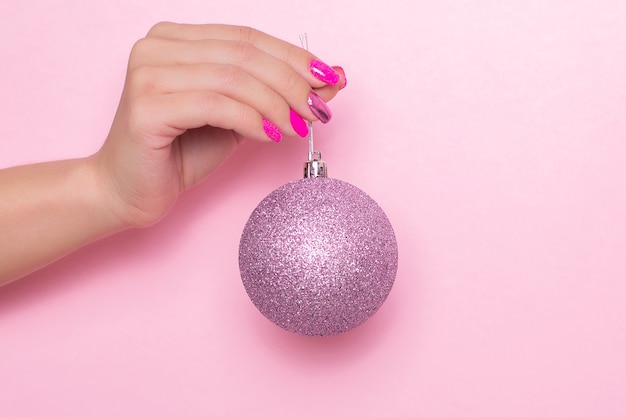 Female hand with festive manicure nails holding Christmas toy