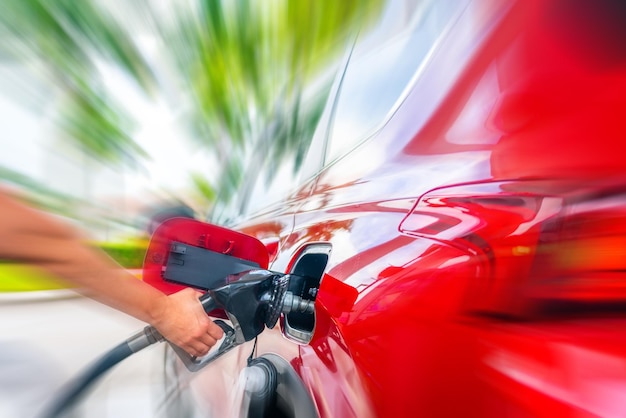 Female Hand with fuel pistol and red car with motion blur effect