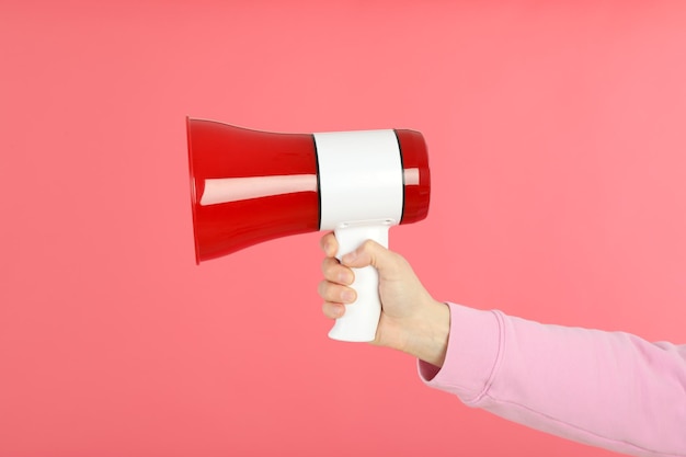 Female hand with megaphone on pink background