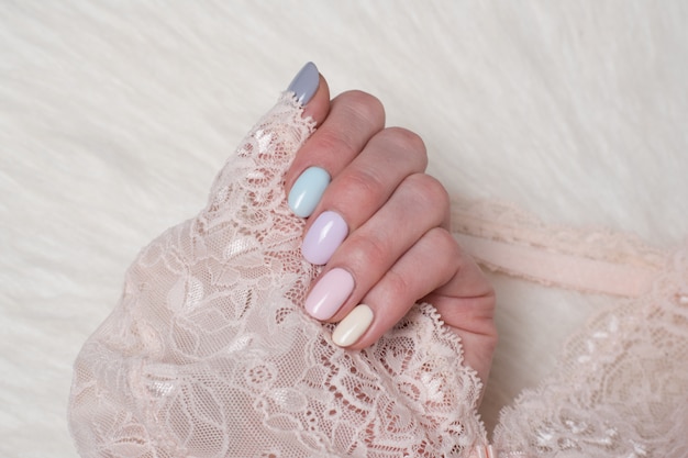 Female hand with a multi-colored gentle manicure. Lace in hand. Close-up